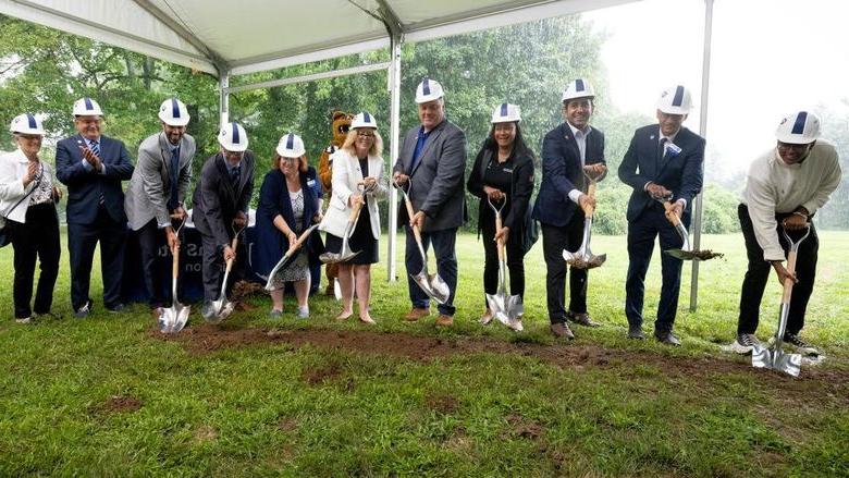 People shoveling dirt under a tent to break ground for new construction